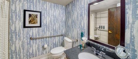 A bathroom with a marble floor, a white toilet, a sink with a mirror, and a framed picture on the wall.