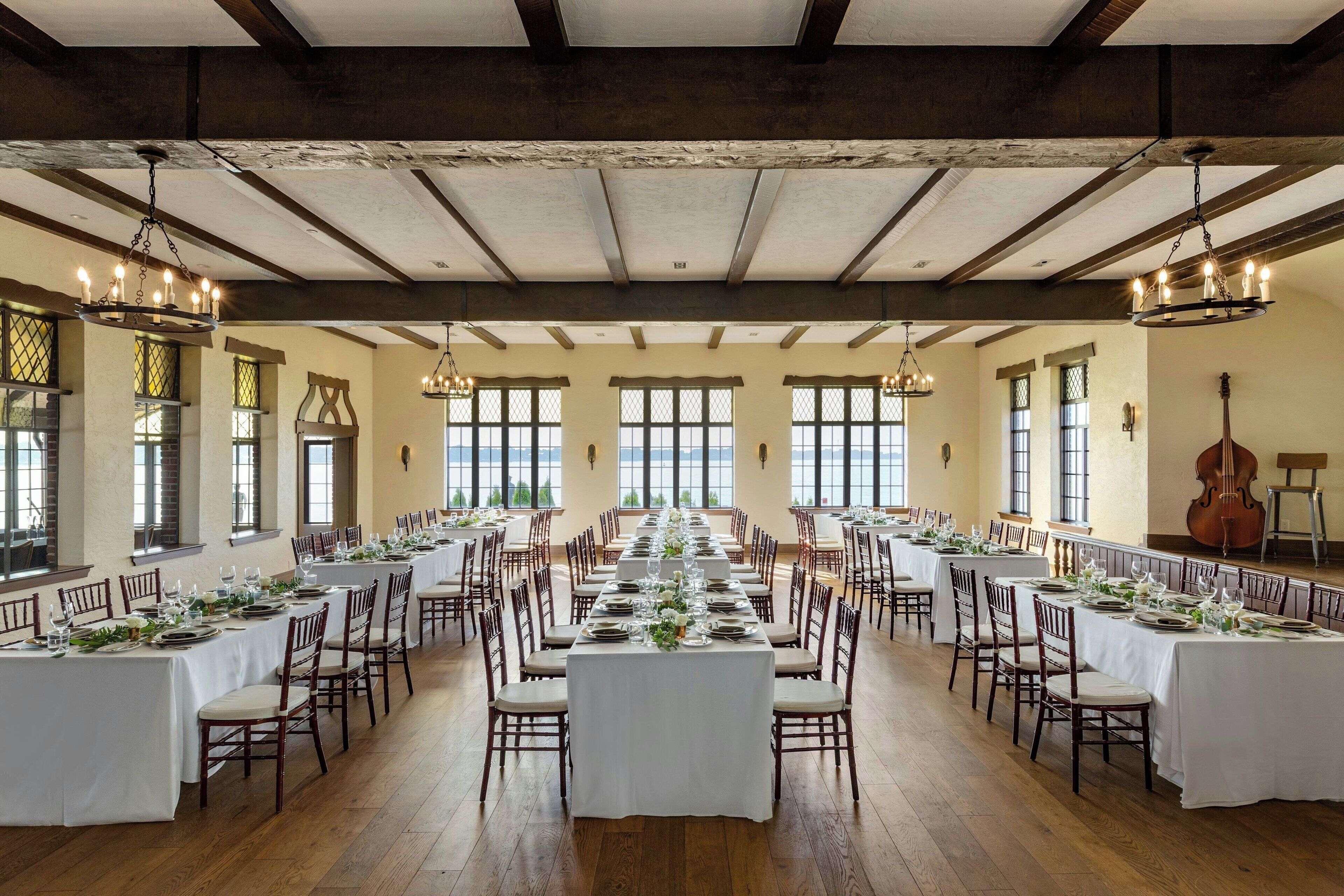Ein großer Festsaal mit langen Tischen zum Essen, Holzbalken an der Decke und großen Fenstern.
