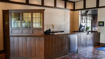 A reception desk with a wooden finish, a glass window, and a small vase with flowers.