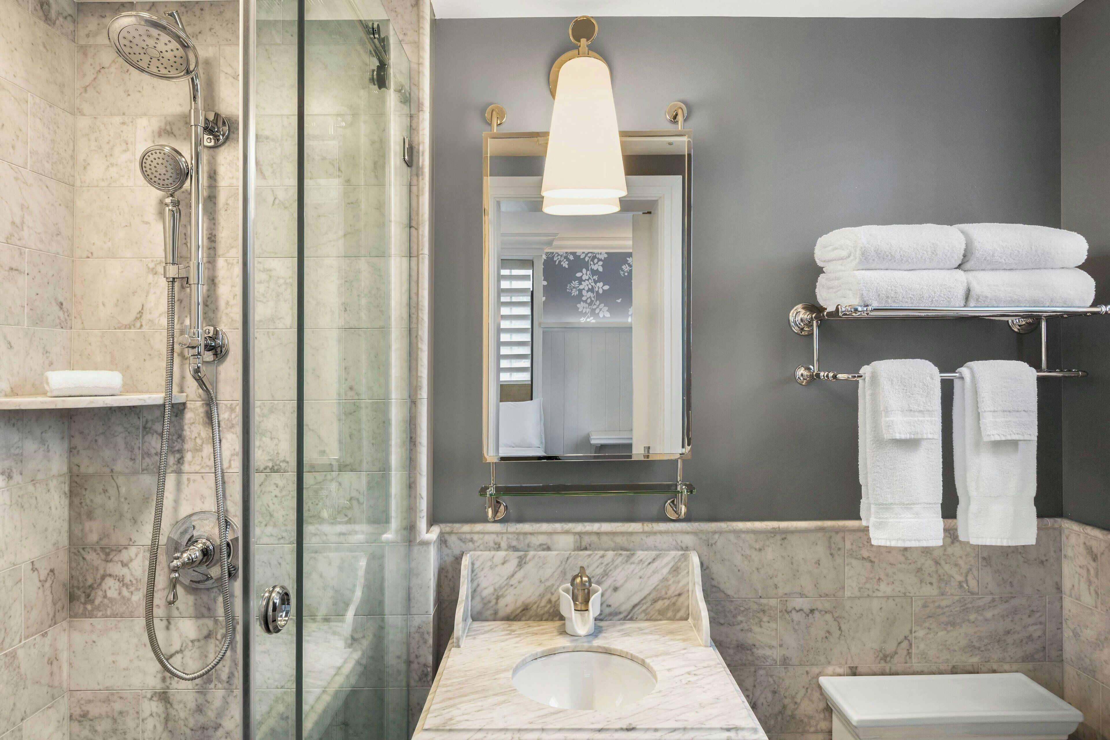 A bathroom with a glass-enclosed shower, a marble sink, and a toilet. There are towels on a rack and a mirror above the sink.