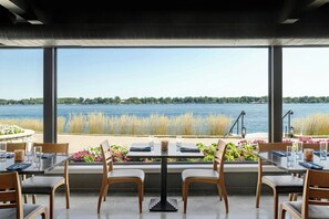 Un área de comedor con mesa y sillas, vista a un lago y barandilla decorada con flores.
