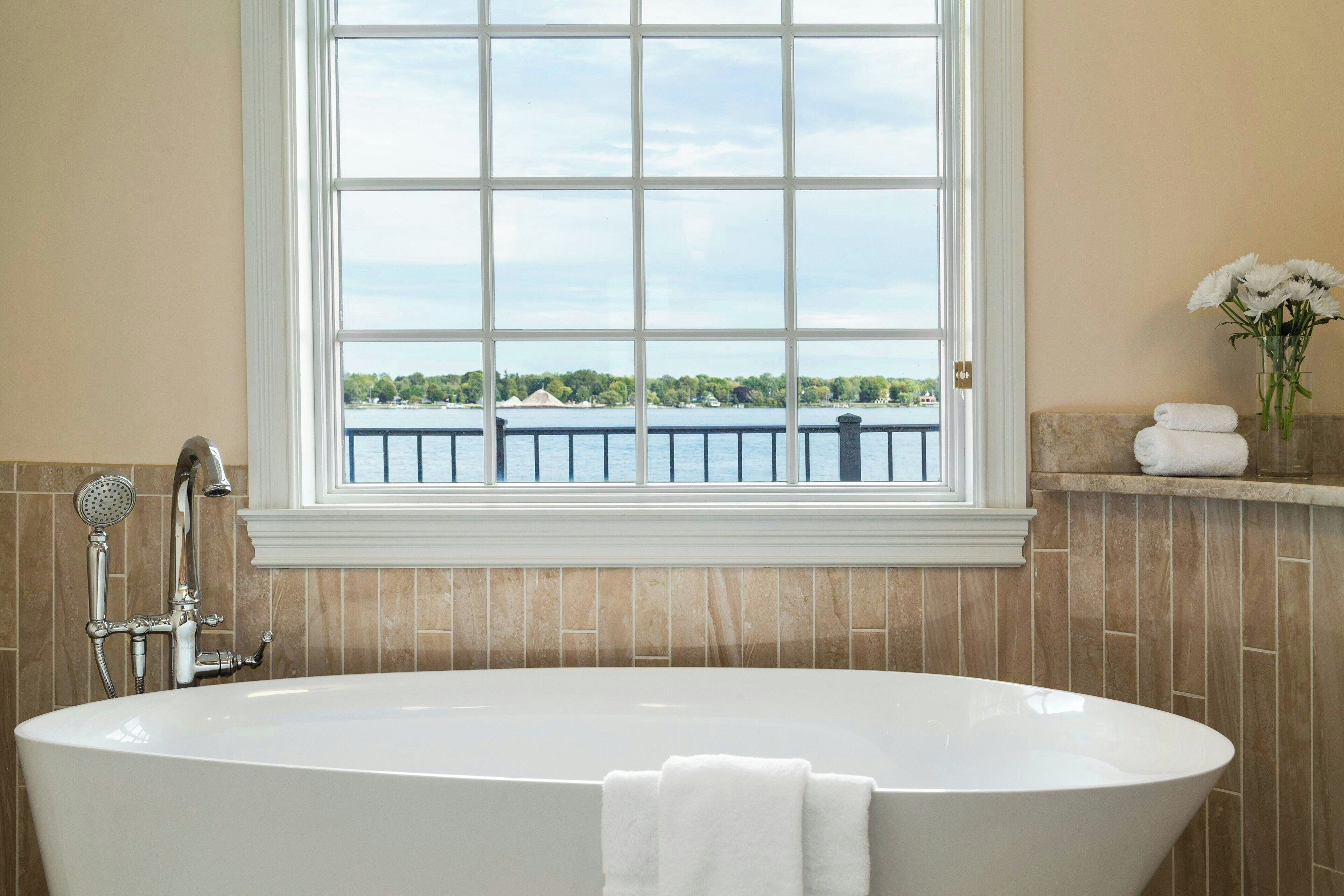 A bathroom with a freestanding bathtub, a window with a view of a body of water and greenery, and a towel rack with folded towels.