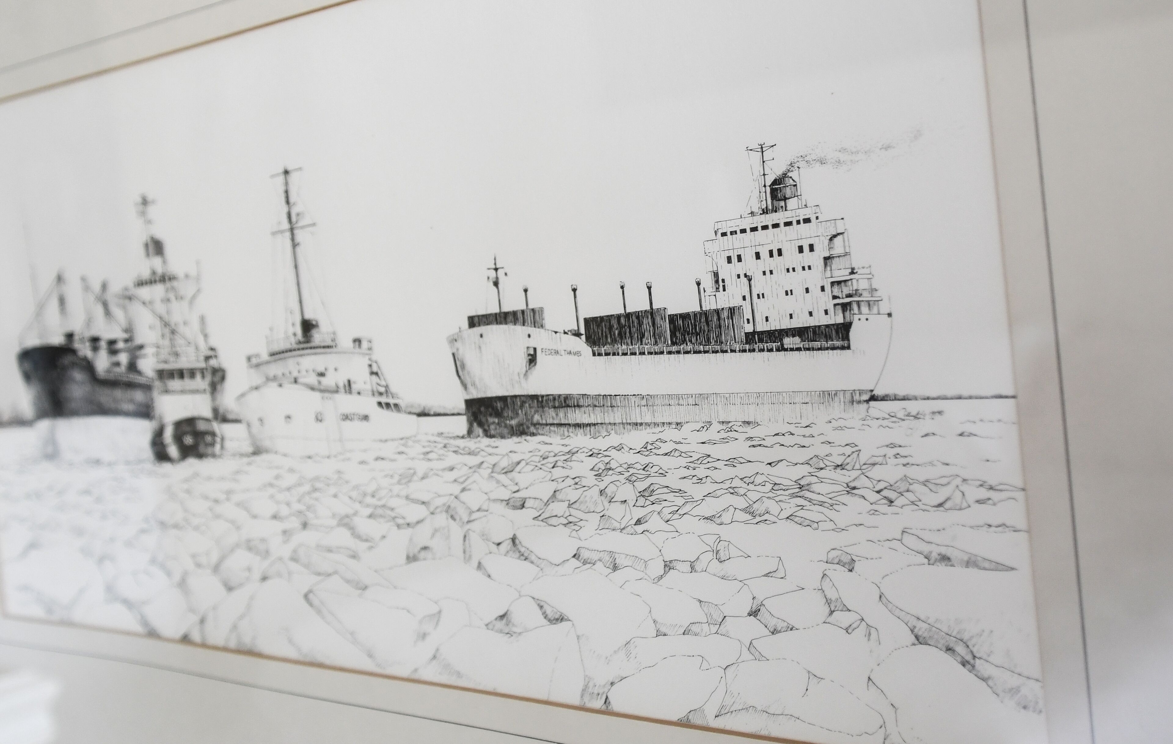 A framed black and white sketch of a ship with a rocky shoreline.