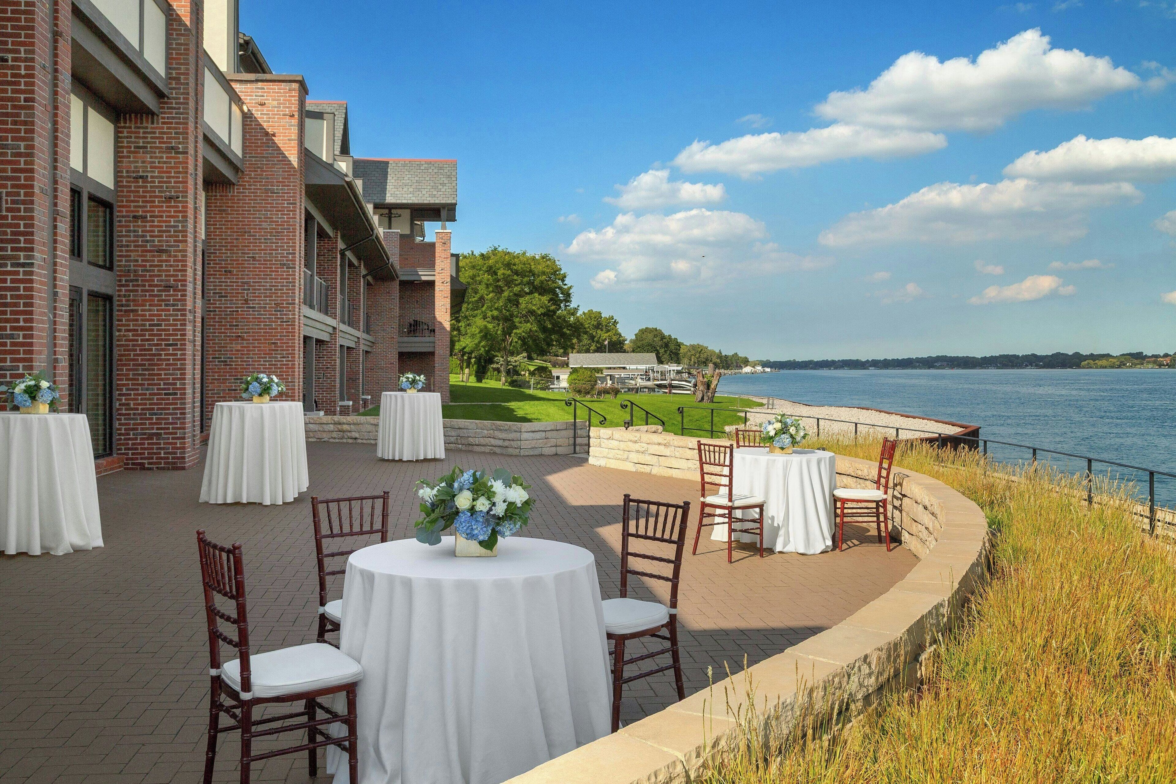 An outdoor patio with round tables and chairs, overlooking a body of water.