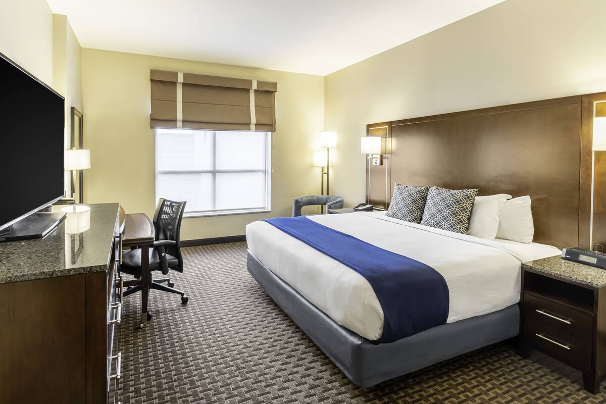 A hotel room with a bed, desk, chair, and a television.