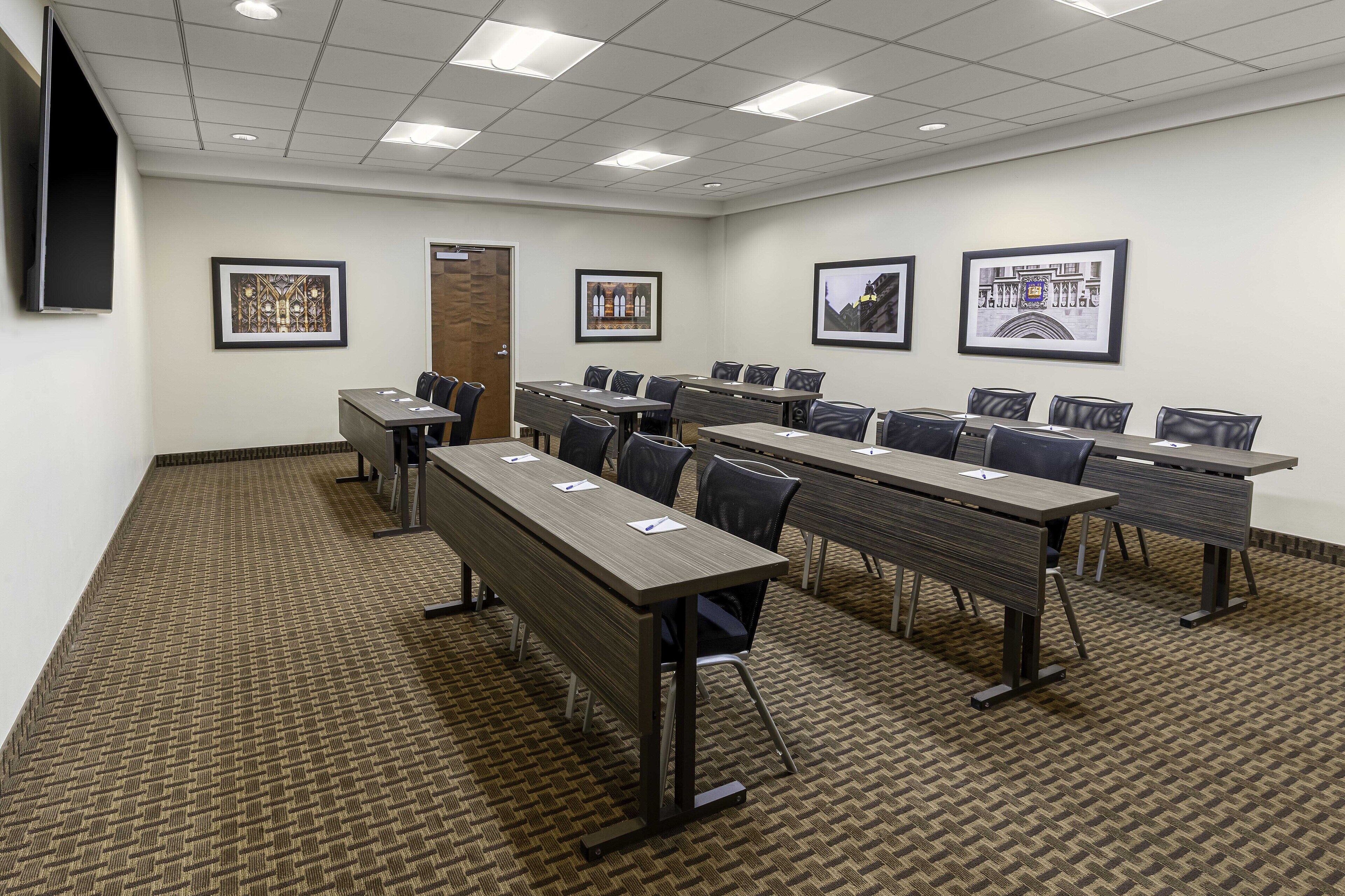 A conference room with multiple tables and chairs, framed pictures on the walls, and a carpeted floor.