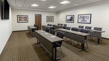 A conference room with multiple tables and chairs, framed pictures on the walls, and a carpeted floor.