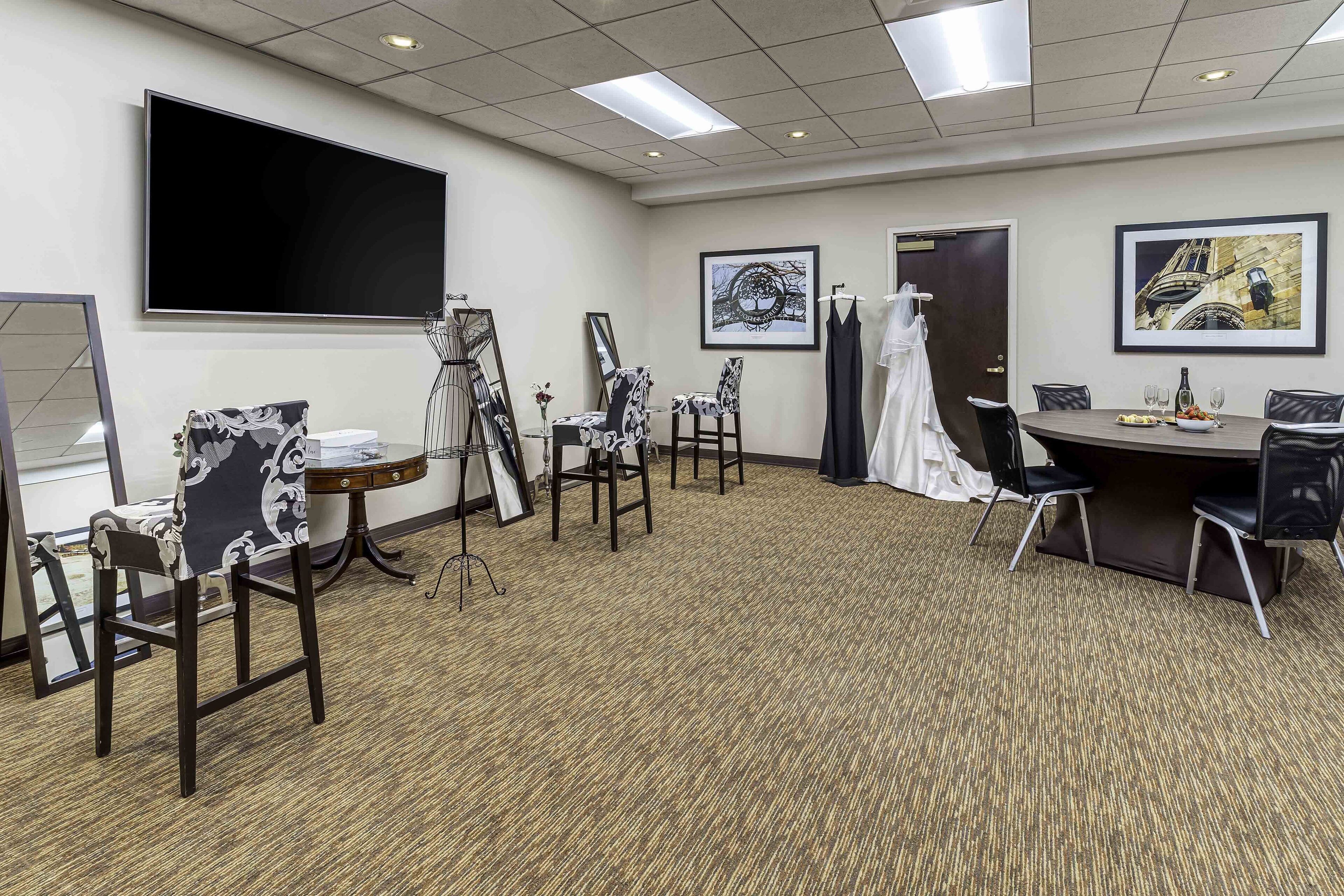 A conference room with a large flat-screen TV, a round table with chairs, and framed artwork on the walls.