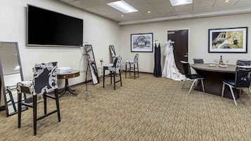 A conference room with a large flat-screen TV, a round table with chairs, and framed artwork on the walls.