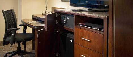 Una habitación de hotel con escritorio, silla, televisor, lámpara y armario.