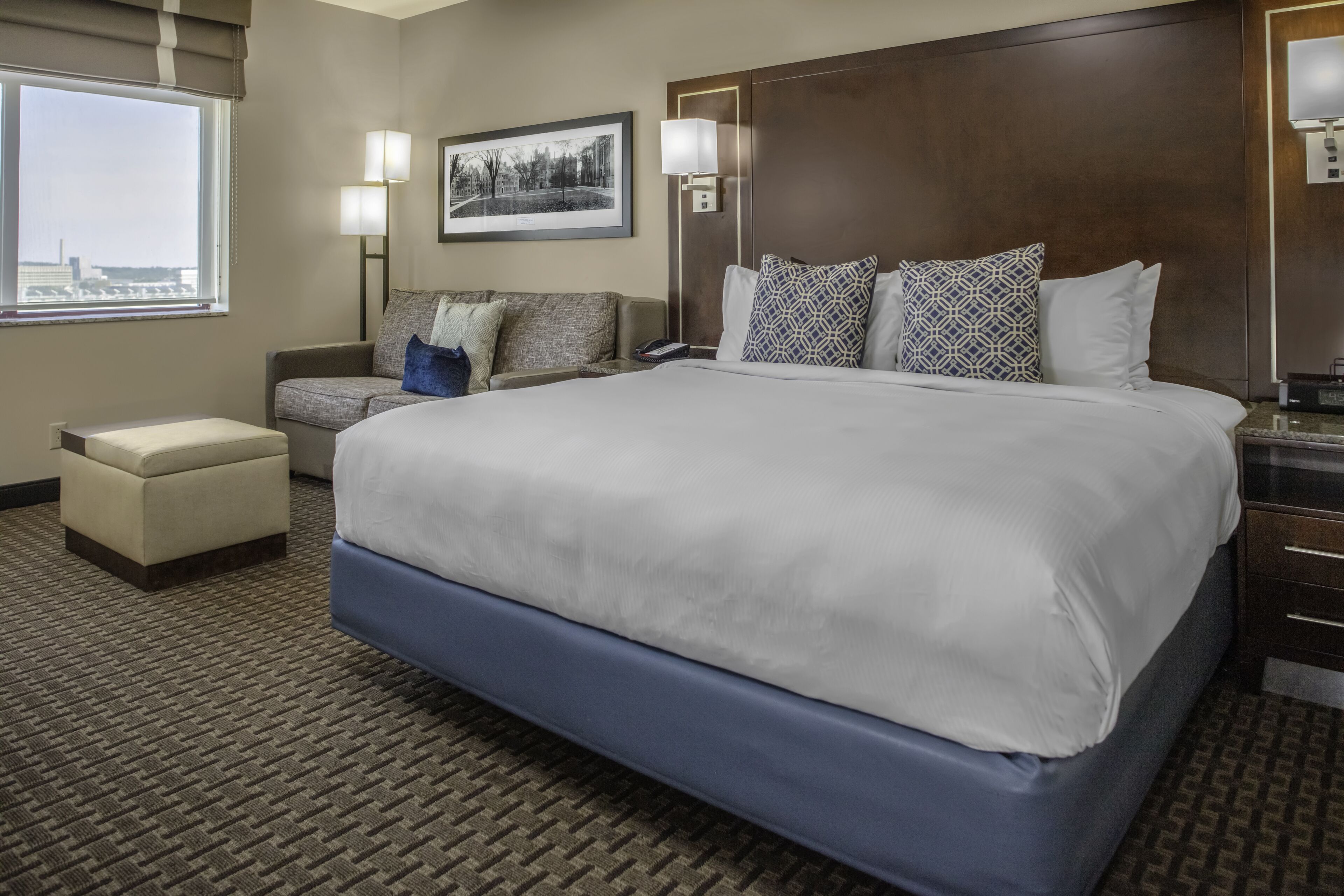 A hotel room with a large bed, a sofa, a small table, and a chair.