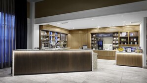 A modern hotel lobby with a reception desk, a coffee station, and a store named "The Market" with various items on display. - New Haven Hotel (New Haven)