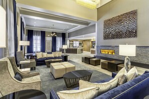 A spacious lobby with a sofa, armchairs, and a coffee table. There is a fireplace and a wall-mounted artwork.