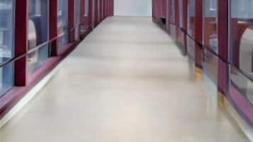 A corridor with glass walls and a metal roof, leading to a large open space.