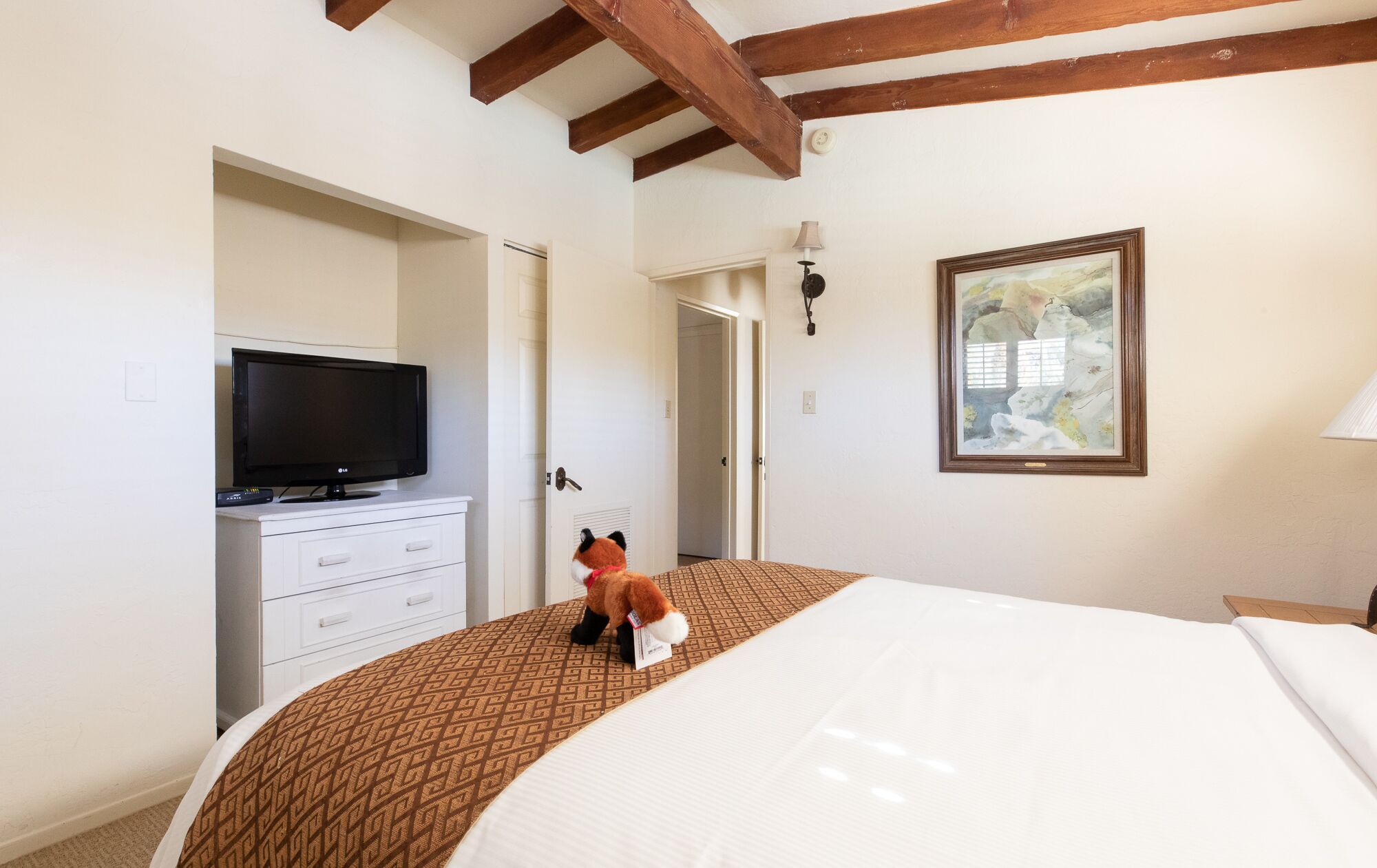 A bedroom with a bed, a television on a dresser, a door, and a framed picture on the wall.