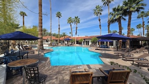 Un espace aménagé au bord de la piscine, avec des chaises longues, des parasols et une piscine à l’eau d’un bleu limpide.