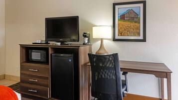 Habitación de hotel con escritorio, televisión, lámpara, silla y un cuadro en la pared.