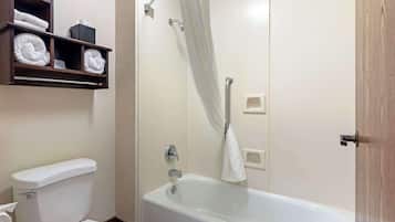 A bathroom with a white bathtub, a toilet, and a shelf with folded towels.