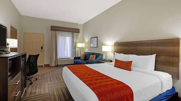 Habitación de hotel con una cama grande, un escritorio con computadora, una silla, un sofá y un televisor.