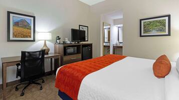 A hotel room with a bed, desk, chair, television, and framed pictures on the walls.