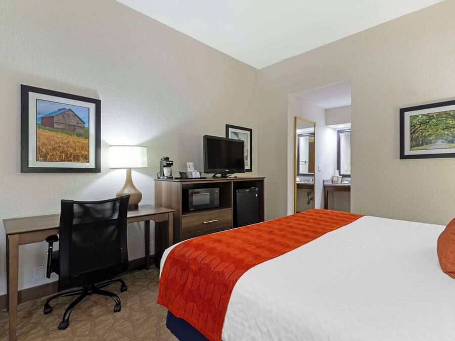A hotel room with a bed, desk, chair, television, and framed pictures on the walls.
