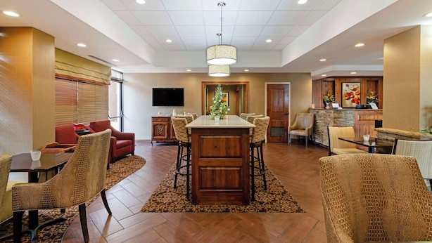 A spacious hotel lobby with a central bar area, seating arrangements, and a television mounted on the wall.