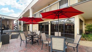 An outdoor patio with brick flooring, tables, chairs, and red umbrellas.
