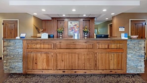 A reception desk with a stone and wood design, a laptop, and two flower arrangements.
