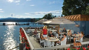 An outdoor dining area with tables and chairs, overlooking a body of water with a dock and mountains in the background. - The Coeur D'alene Golf and Spa Resort (Coeur d'Alene)