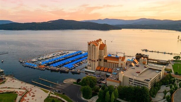 A marina with boats, a hotel with a red roof, and a mountainous backdrop. - The Coeur D'alene Golf and Spa Resort (Coeur d'Alene)
