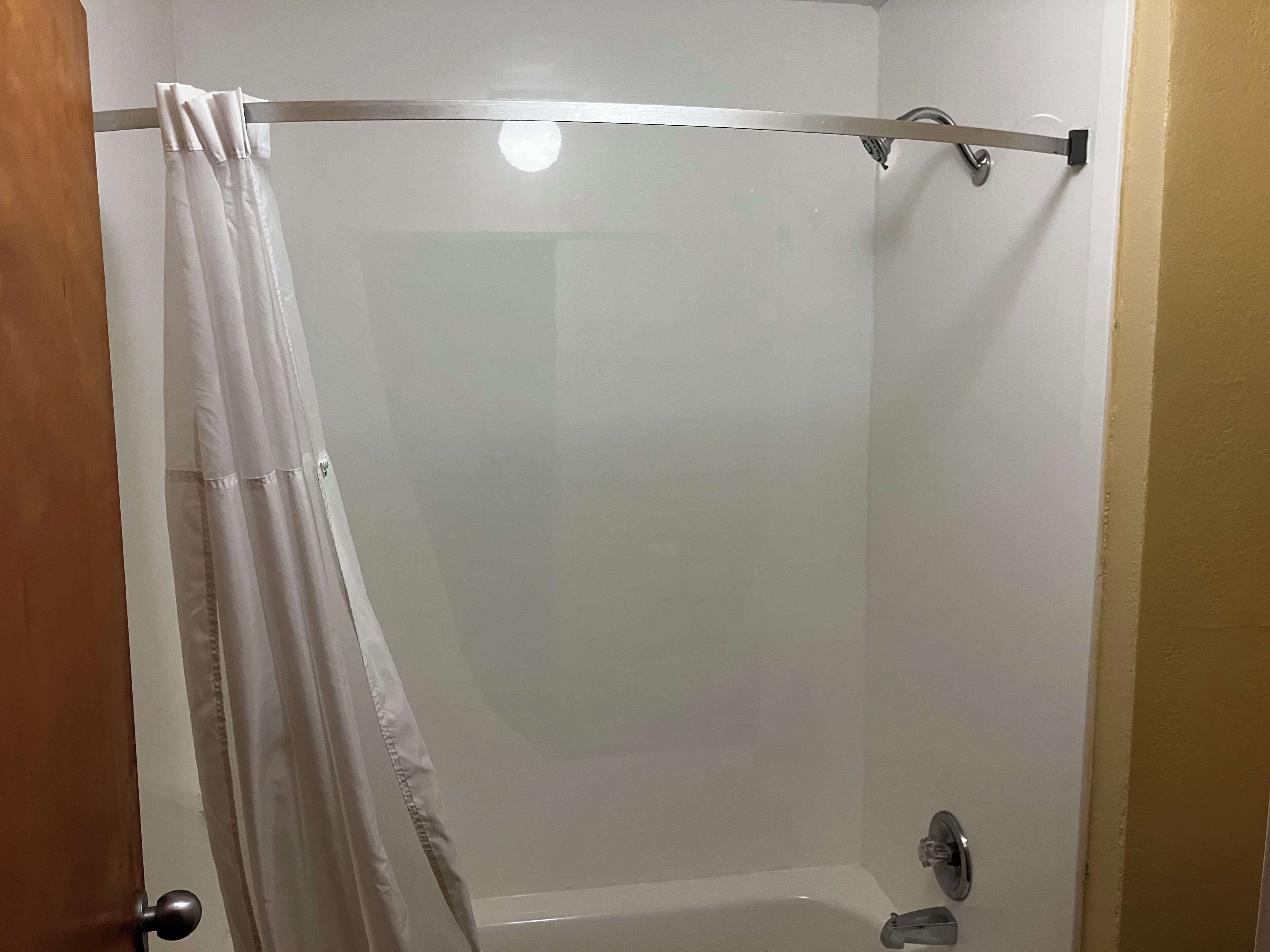 A shower with a white curtain, a handheld showerhead, and a wall-mounted faucet.
