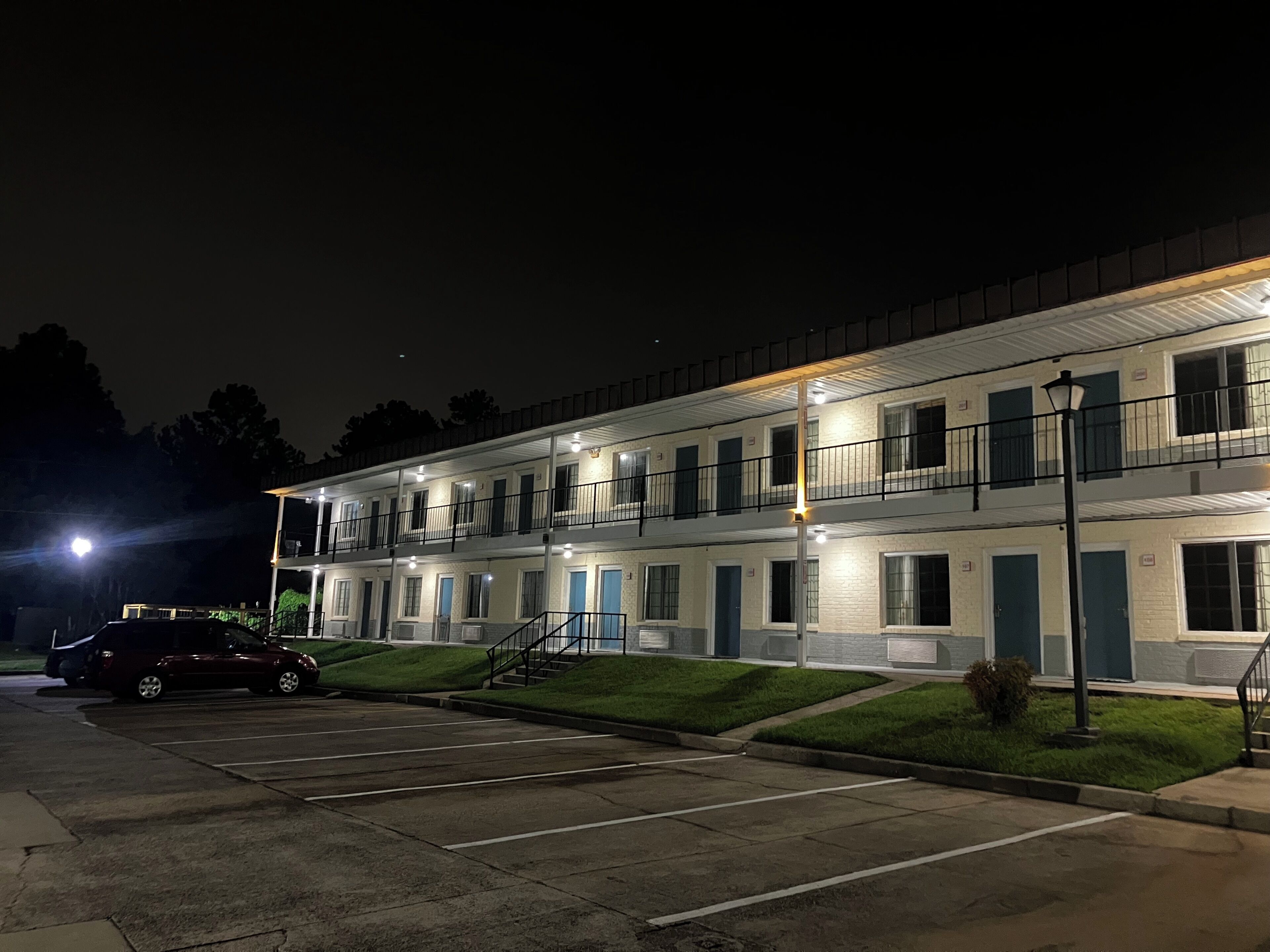 A multi-story motel with a parking lot, a staircase, and a street lamp.