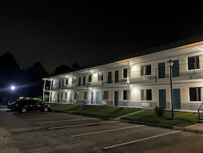 A multi-story motel with a parking lot, a staircase, and a street lamp.
