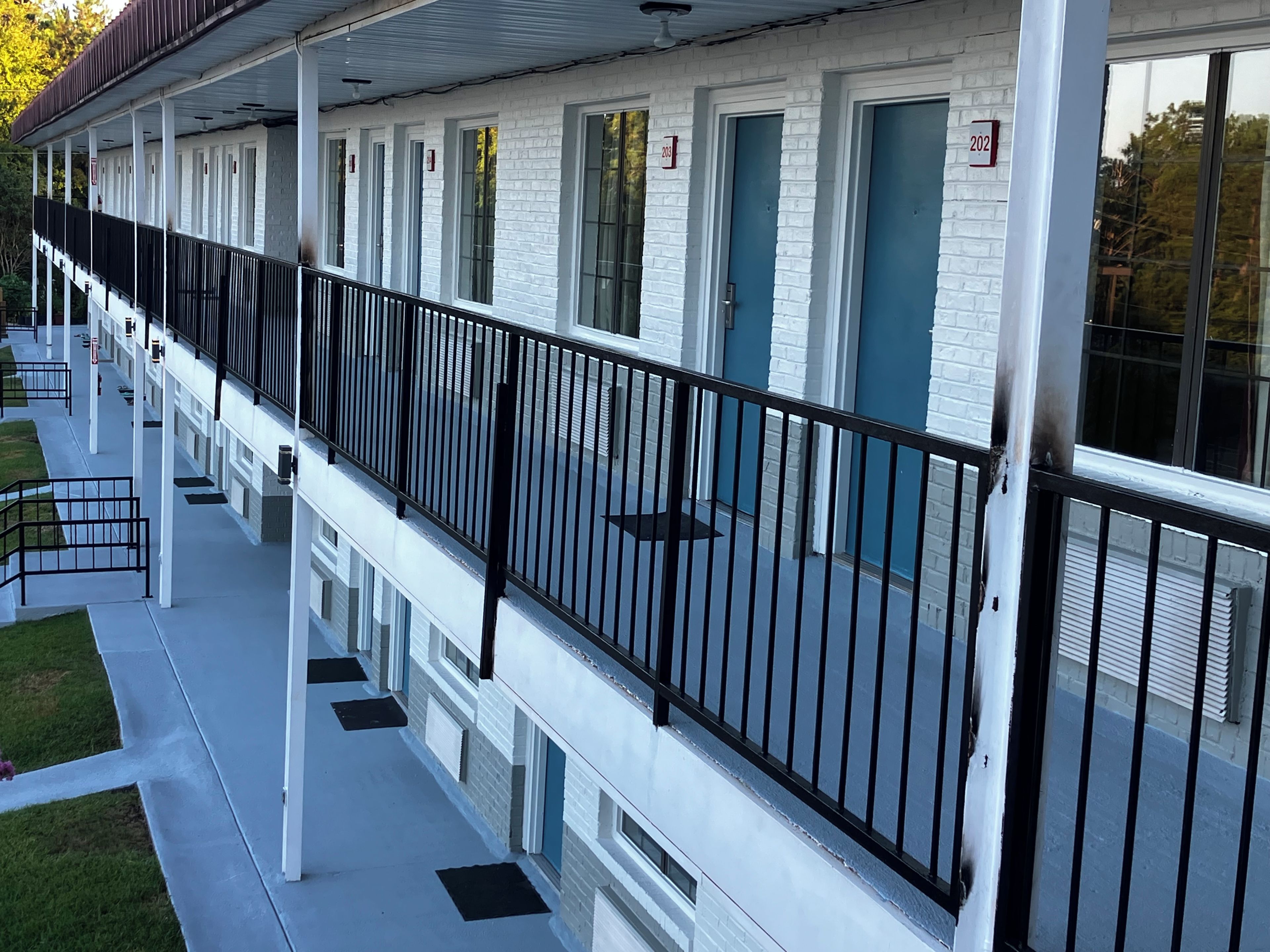 Una hilera de habitaciones de hotel con puertas individuales, un corredor cubierto y una barandilla de metal negro.