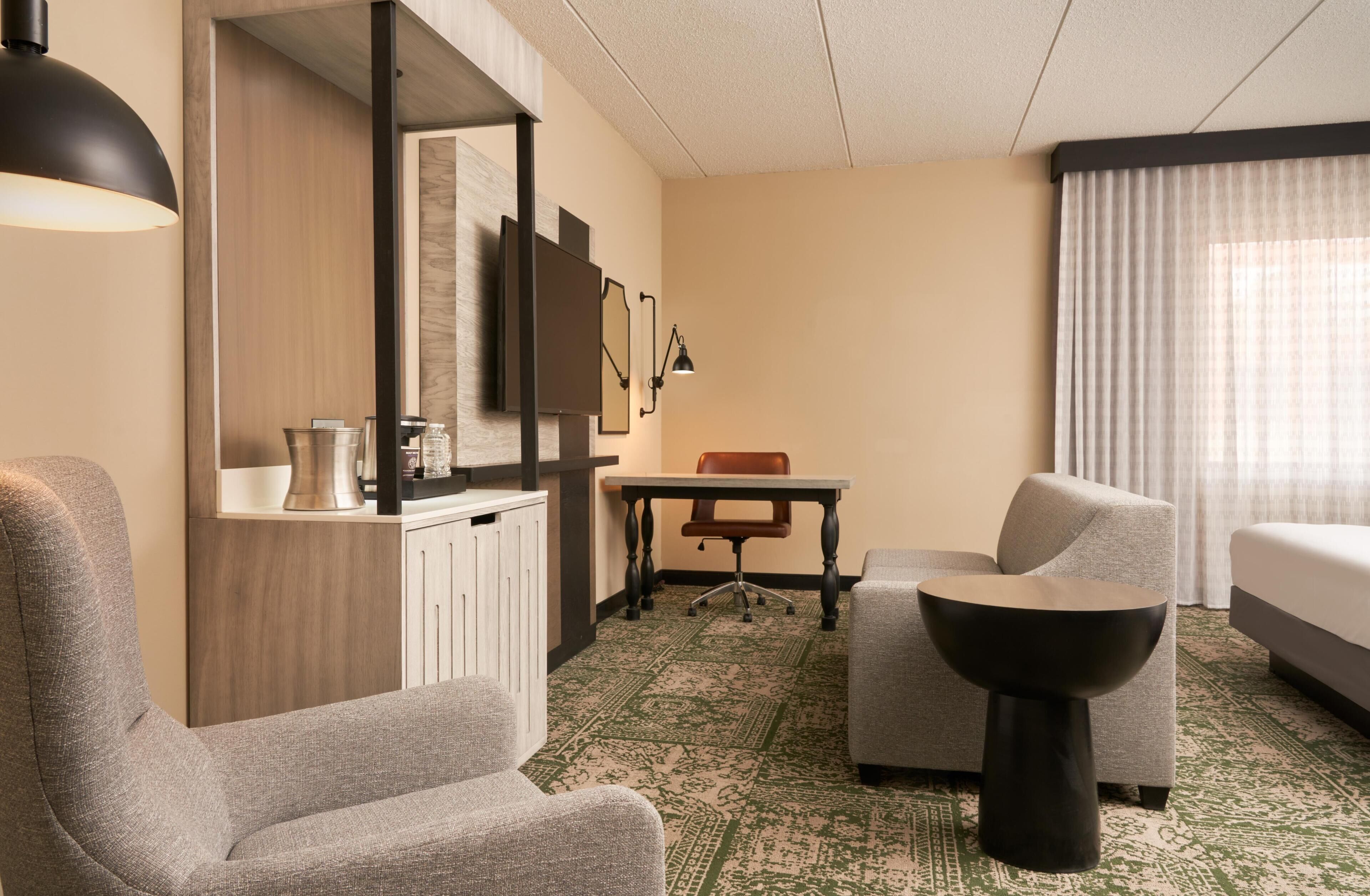 Una habitación de hotel con cama, dos sillones, una mesita, un escritorio, un televisor y una cafetera.