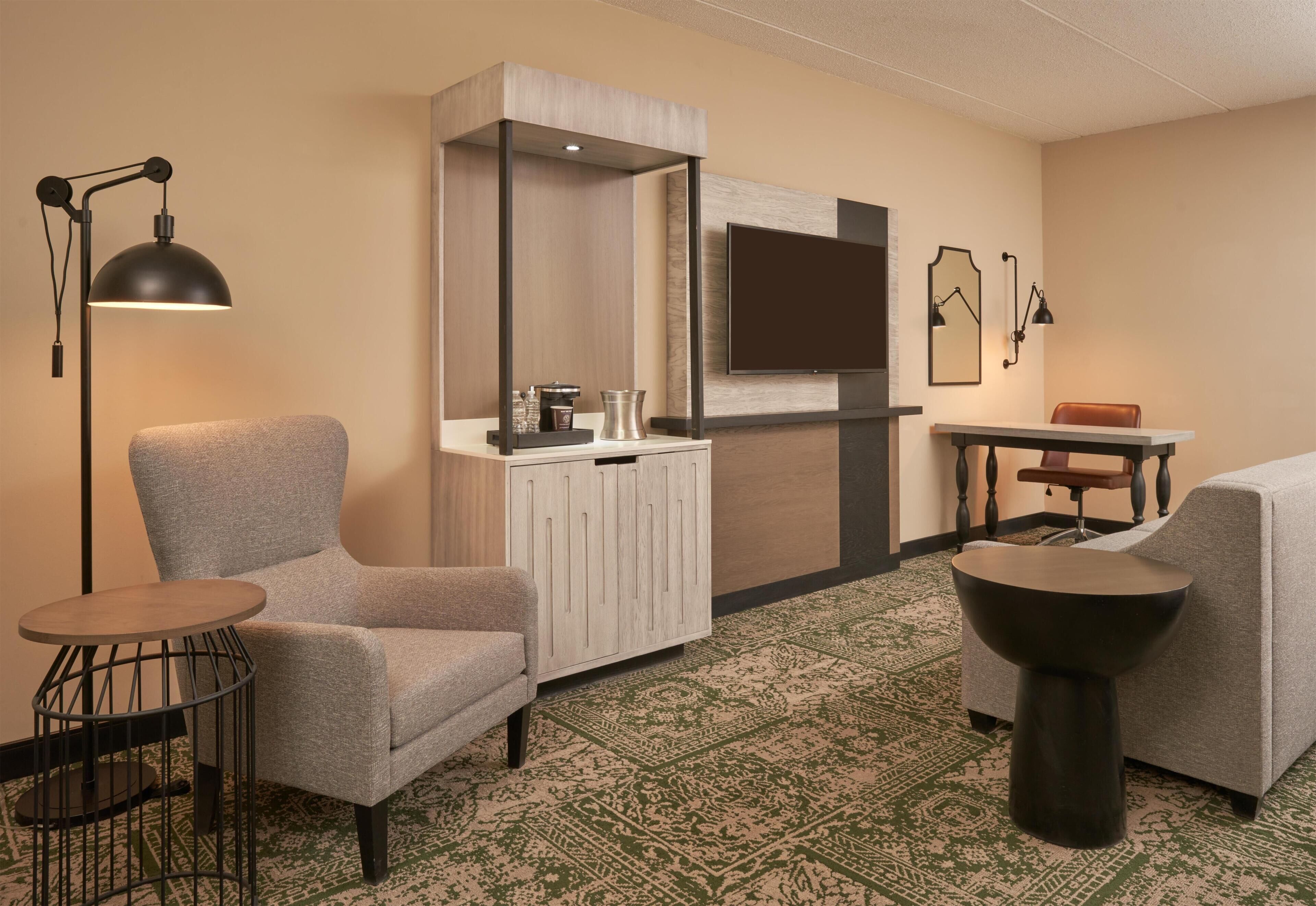 Une chambre d’hôtel équipée d’un canapé, d’un fauteuil, d’une petite table et d’un téléviseur fixé au mur.