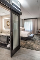 Habitación de hotel con una cama grande, baño independiente con tocador, escritorio y ventana con cortinas.