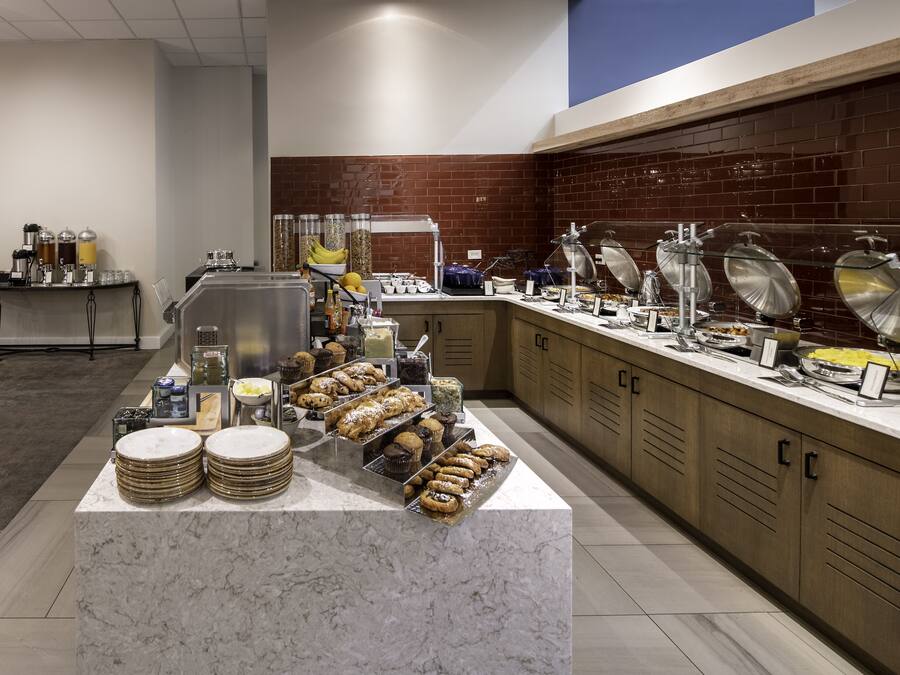 A buffet setup with various food items and beverages, including pastries and drinks, arranged on a marble counter.