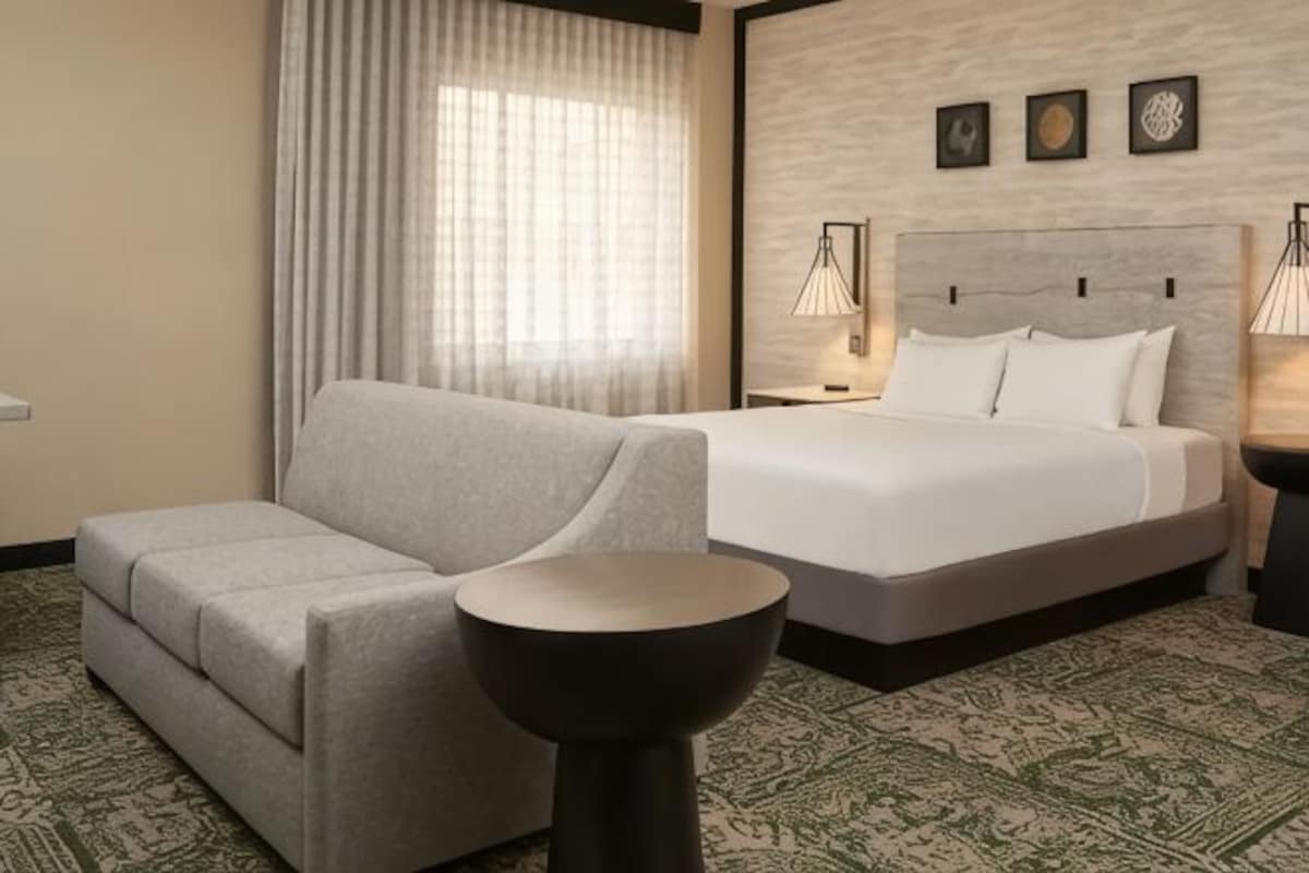 A hotel room with a bed, a sofa, a round table, and a patterned carpet.