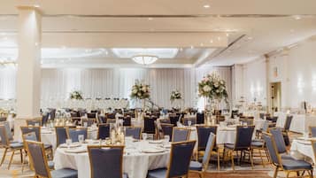 A banquet hall with round tables, chairs, and floral centerpieces.