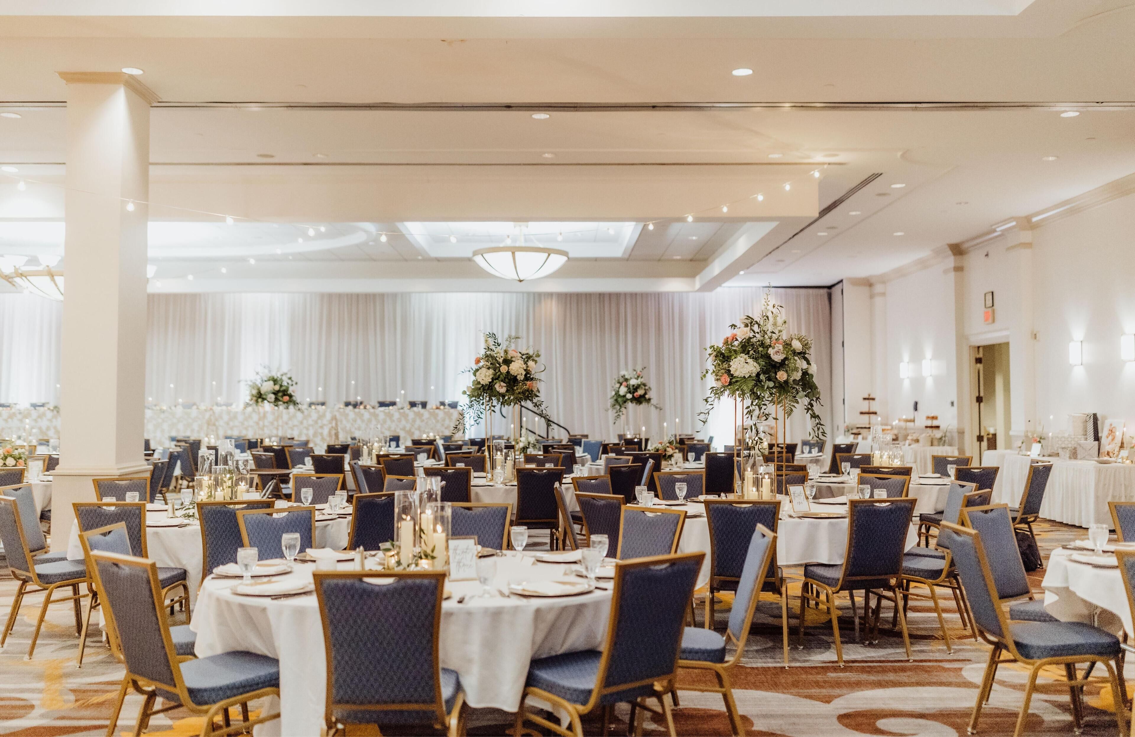Un salón de banquetes con mesas redondas, sillas y centros de mesa florales.