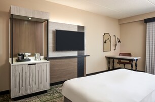 Una habitación de hotel con cama, televisor montado en la pared, escritorio con silla y un minibar.