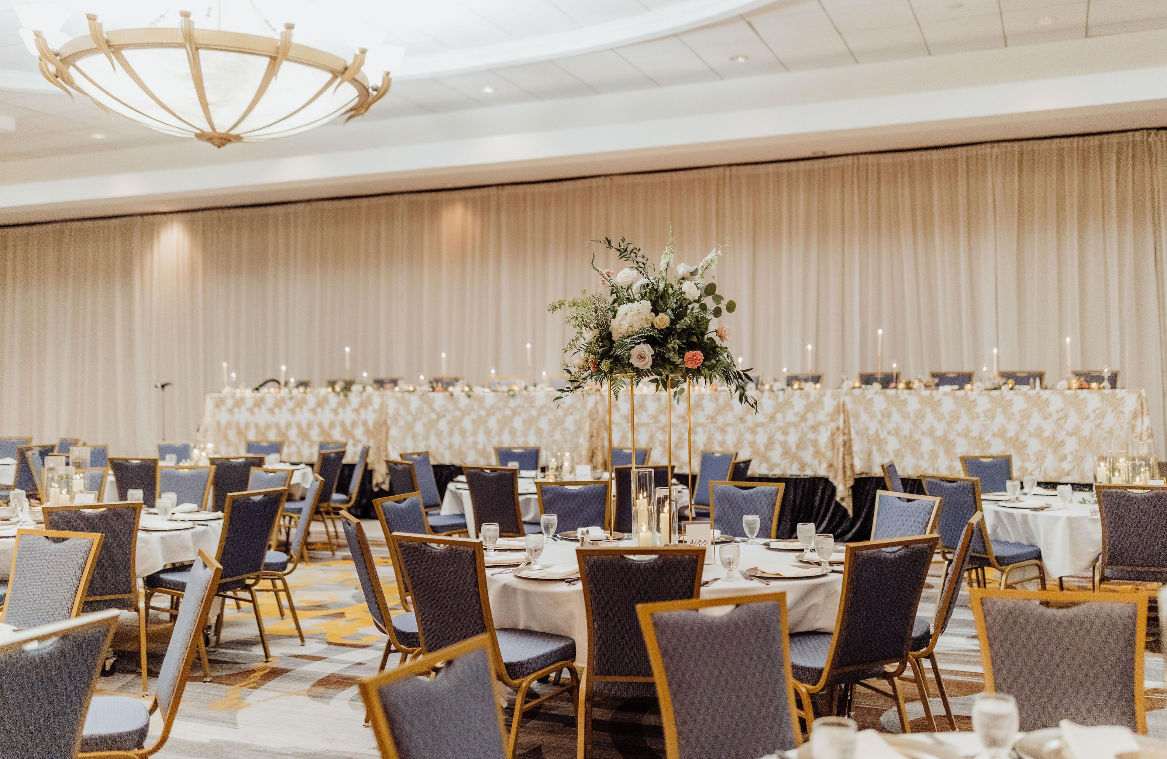 A banquet hall with round tables, chairs, and a central floral arrangement.
