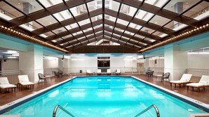 An indoor swimming pool with a high ceiling and skylights, surrounded by lounge chairs and a tiled floor. - Hilton Appleton Paper Valley (Appleton)