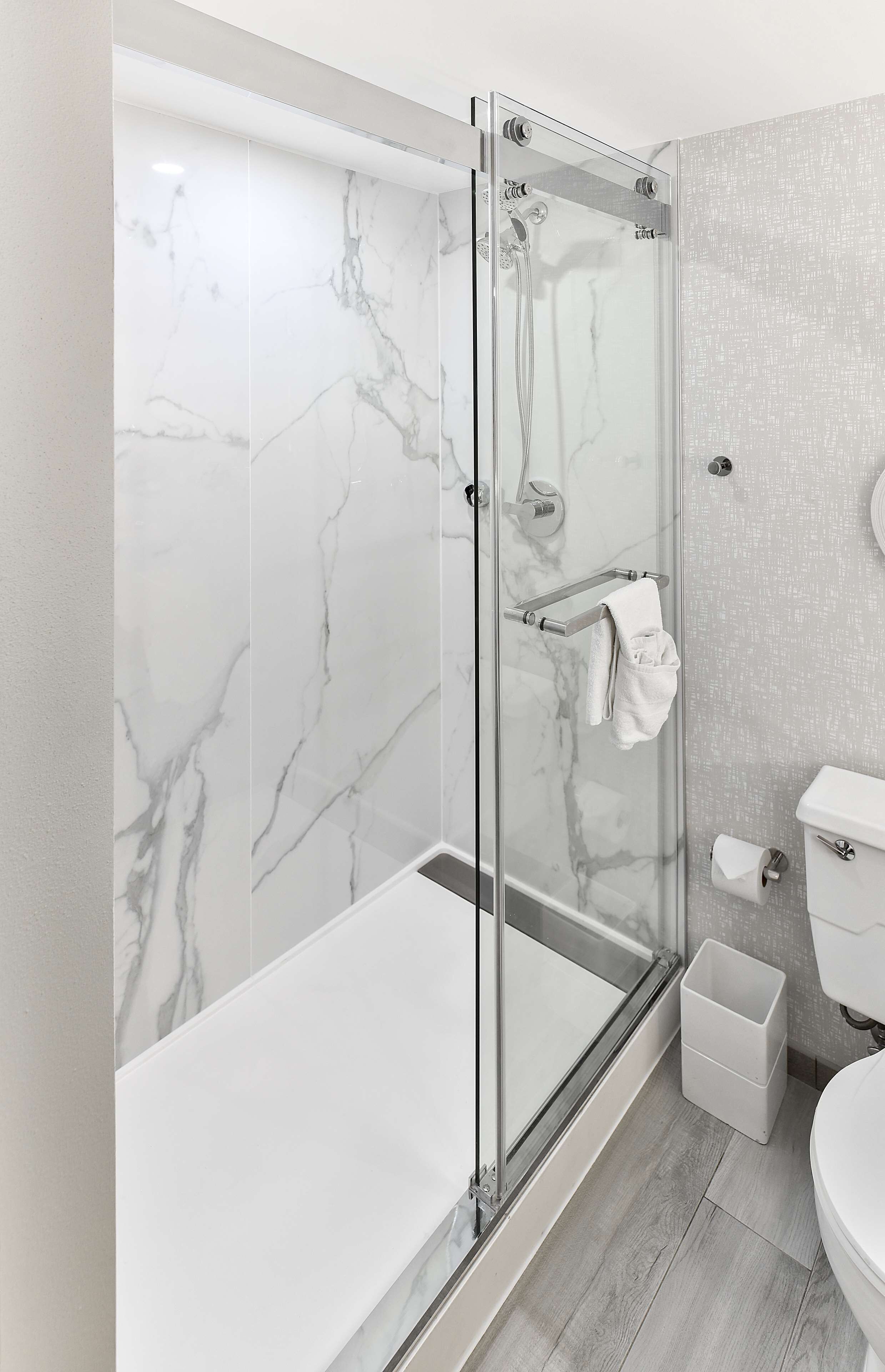 A modern bathroom with a glass-enclosed shower, marble walls, and a white toilet.