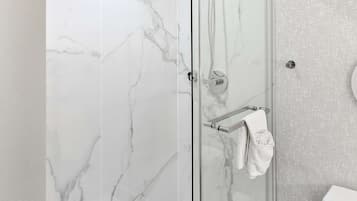 A modern bathroom with a glass-enclosed shower, marble walls, and a white toilet.