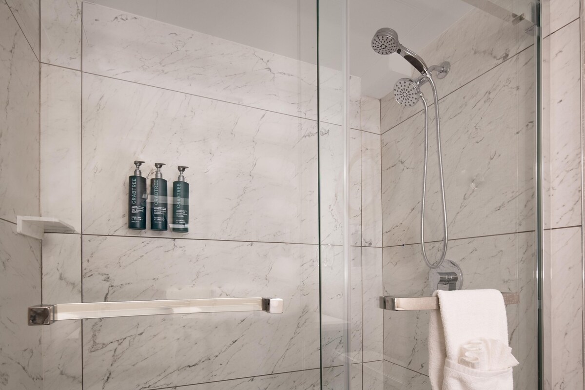 A modern bathroom with a glass-enclosed shower, marble tiles, and a towel rack.