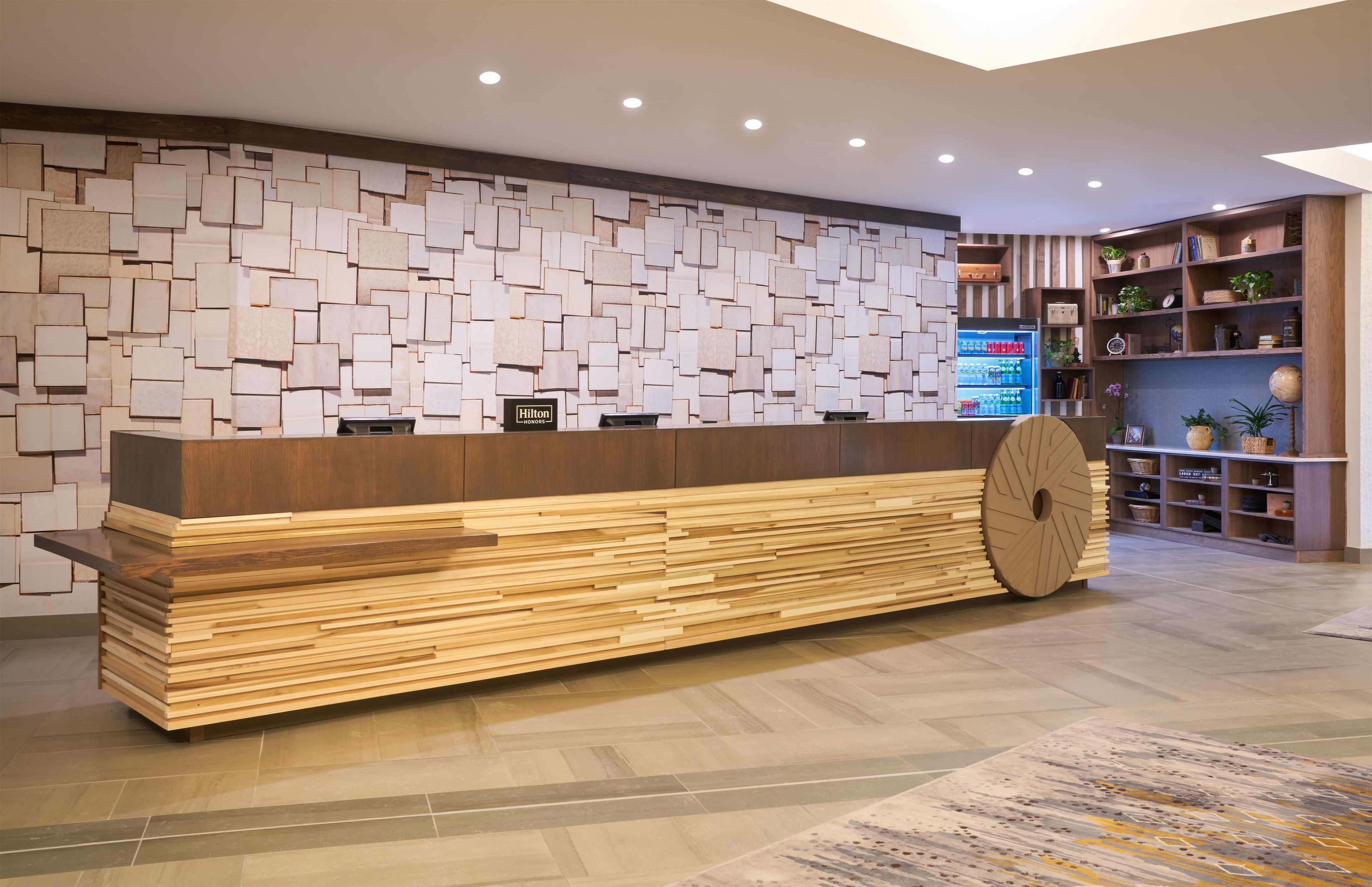 A hotel reception desk with a modern design, a large wooden counter, and a wall with a geometric pattern.