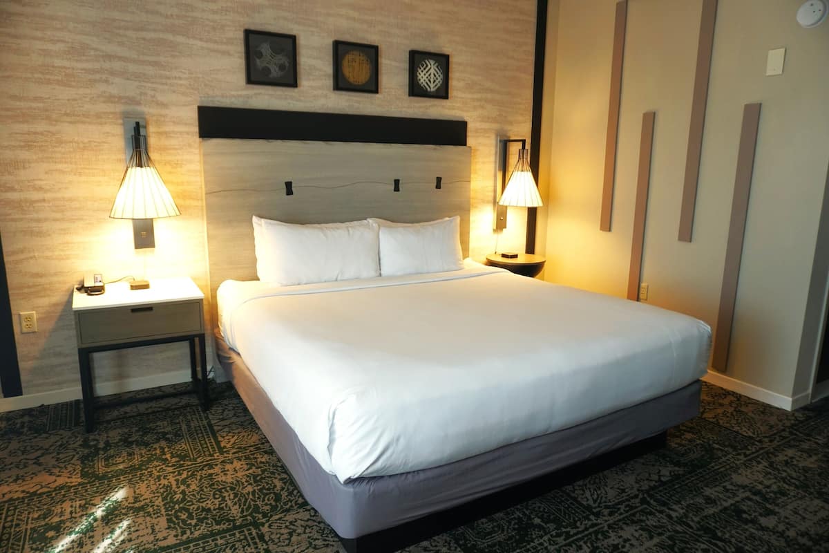 A neatly made bed with white linens, two bedside lamps, a nightstand, and a wall with three framed pictures.