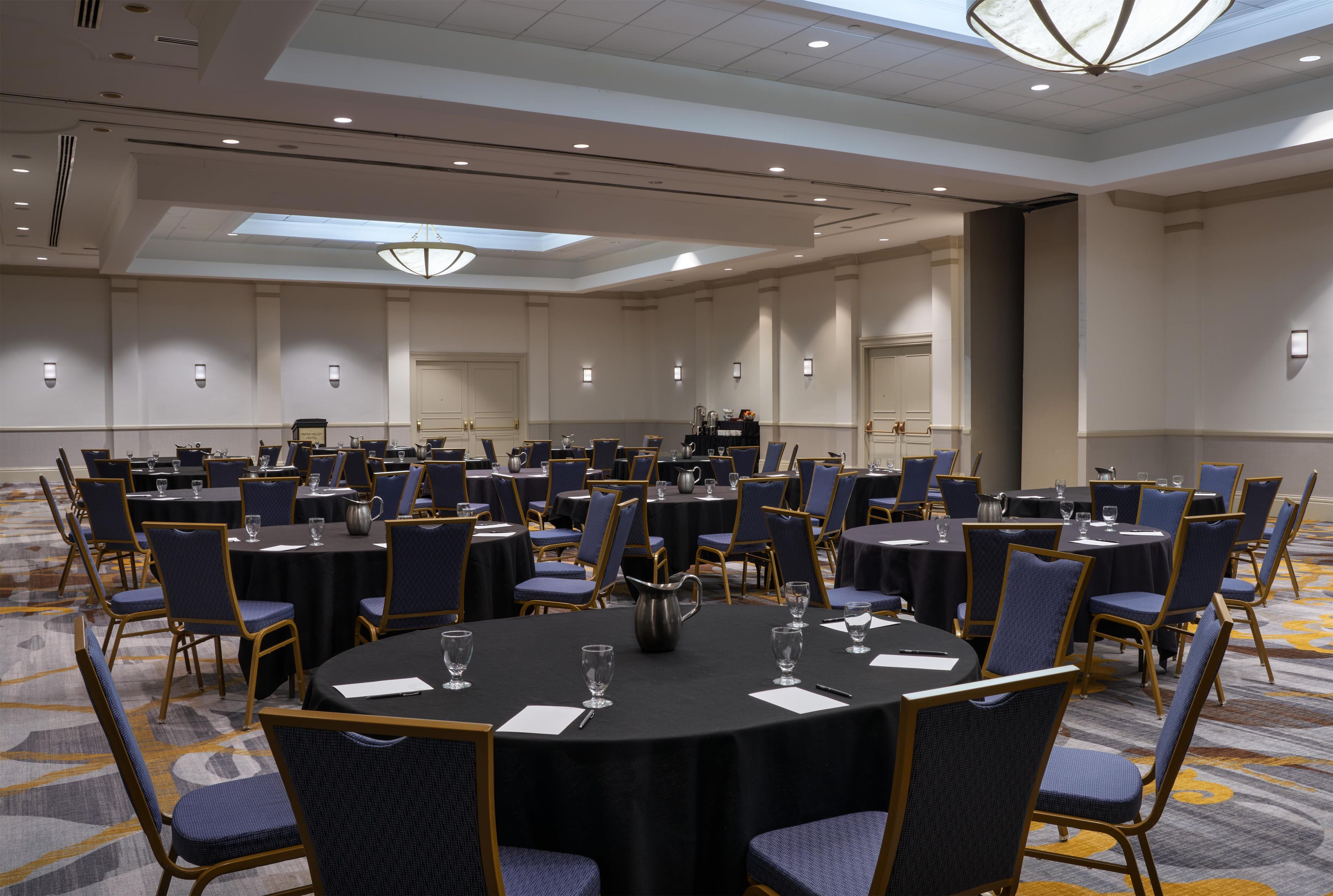 Une salle de conférence équipée de tables rondes, de chaises et d’une scène.